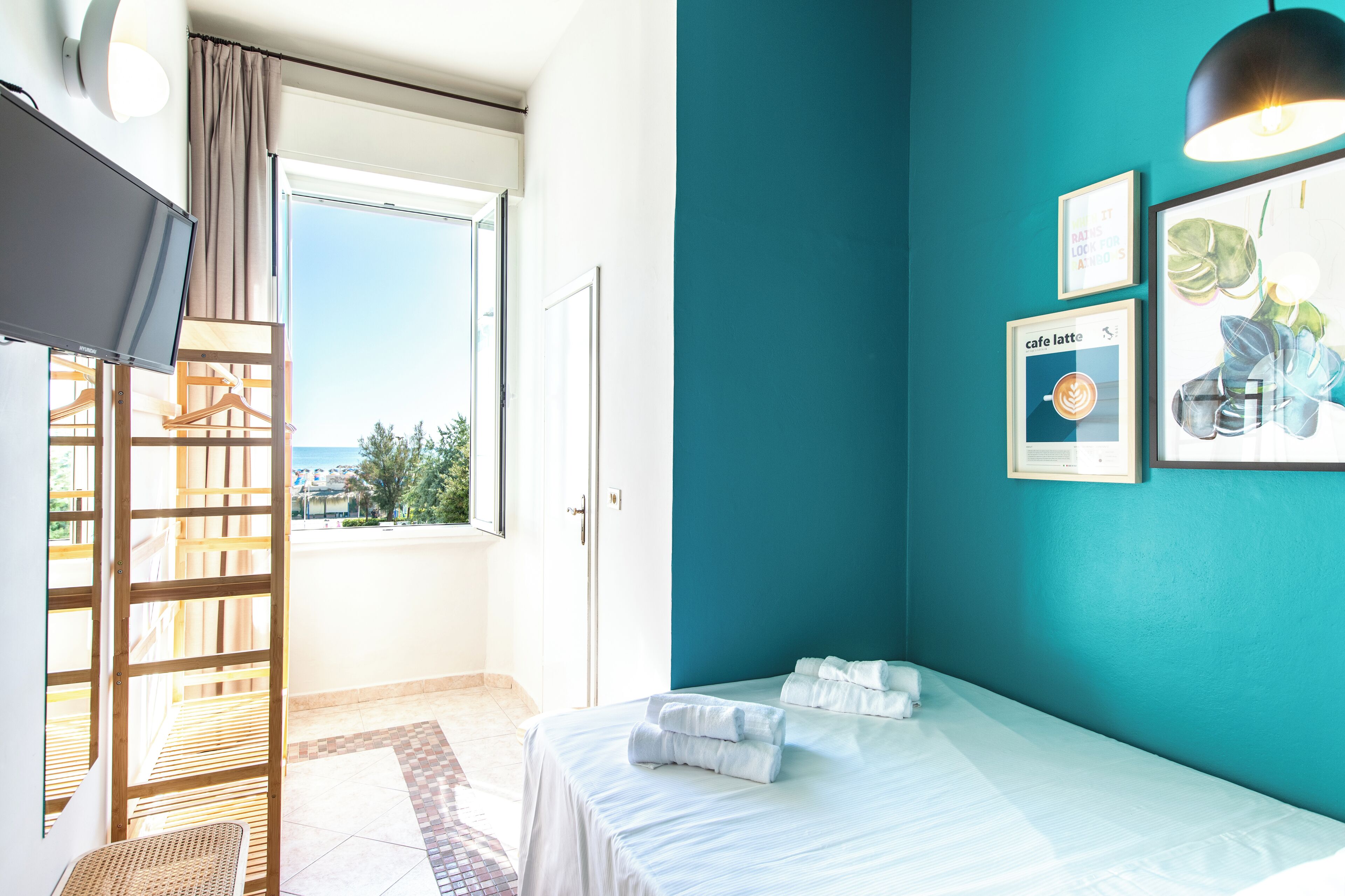 A hotel room with a bed, a TV, a window with curtains, and a balcony.