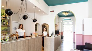 A reception area with a counter, two staff members, a coffee station, and a seating area with a view of the hallway. - Hotel Belvedere Rimini (Rimini)