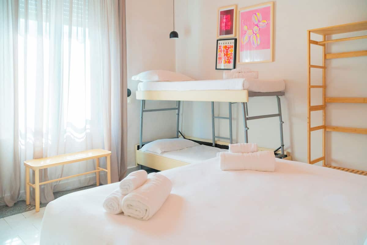 A bunk bed room with a wooden bench, a bedside table, and a framed picture on the wall.