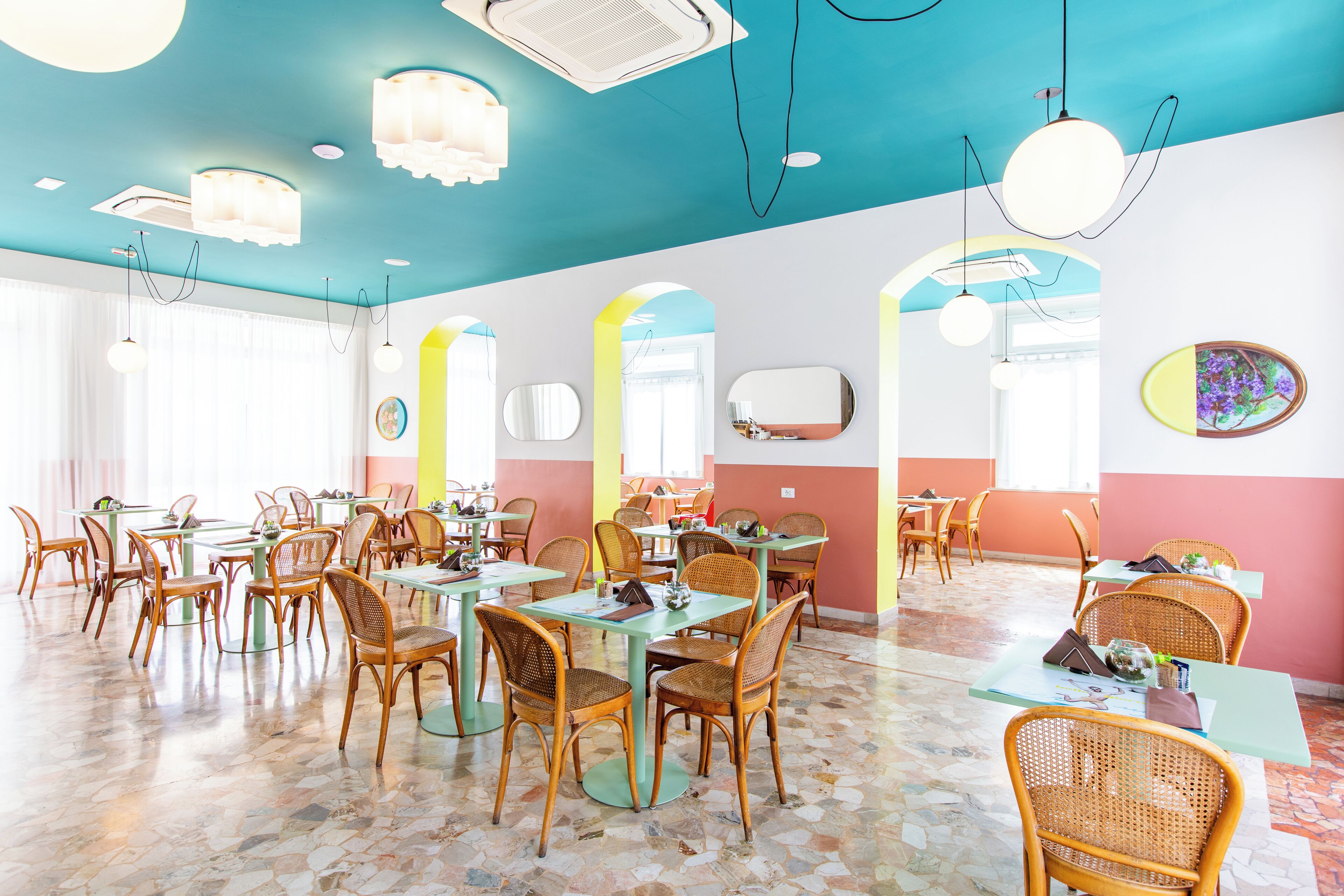 Ein Restaurant mit mehreren Tischen und Stühlen, einem gefliesten Boden und einer farbenfrohen Decke.