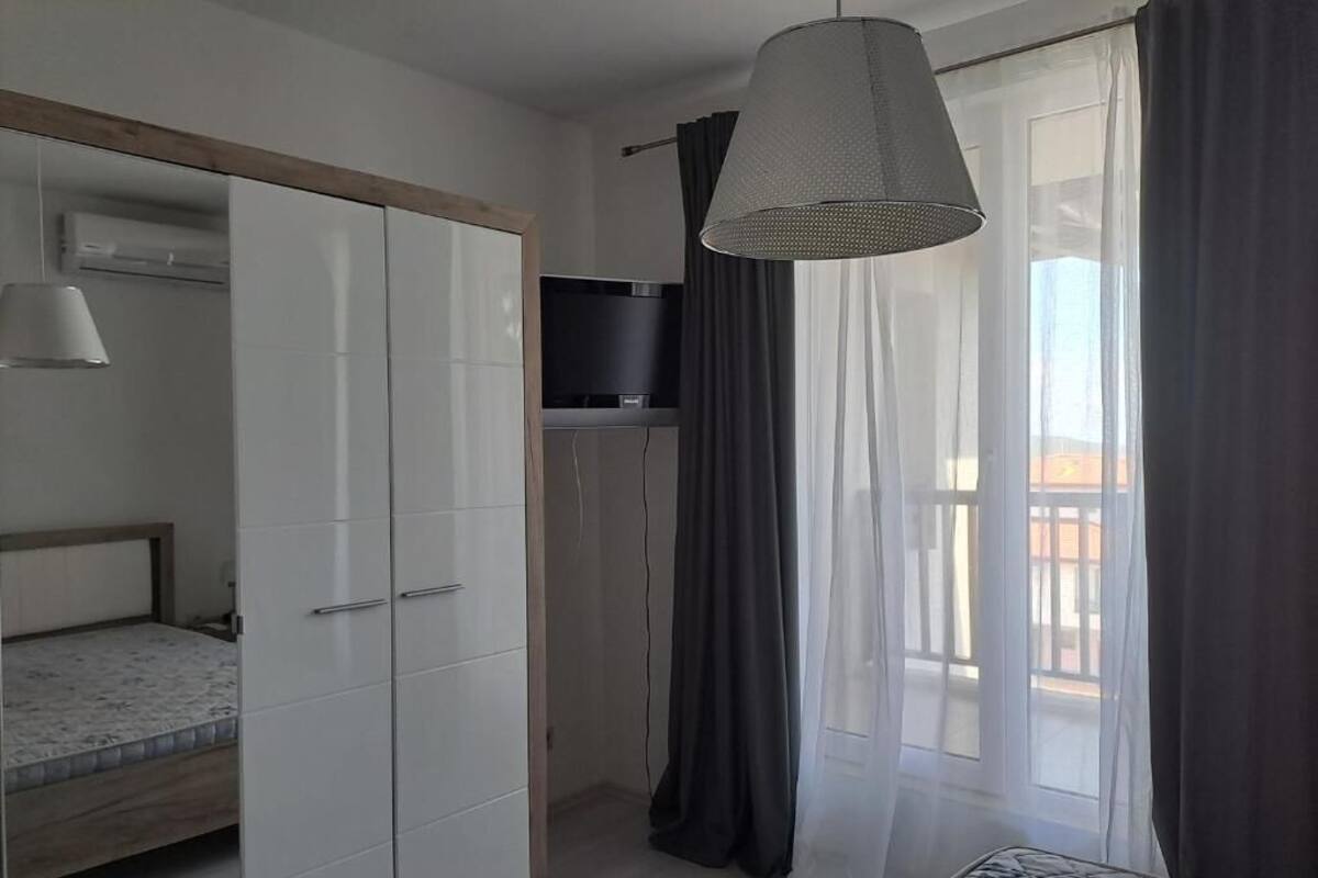 A bedroom with a bed, wardrobe, TV, and a balcony with curtains.