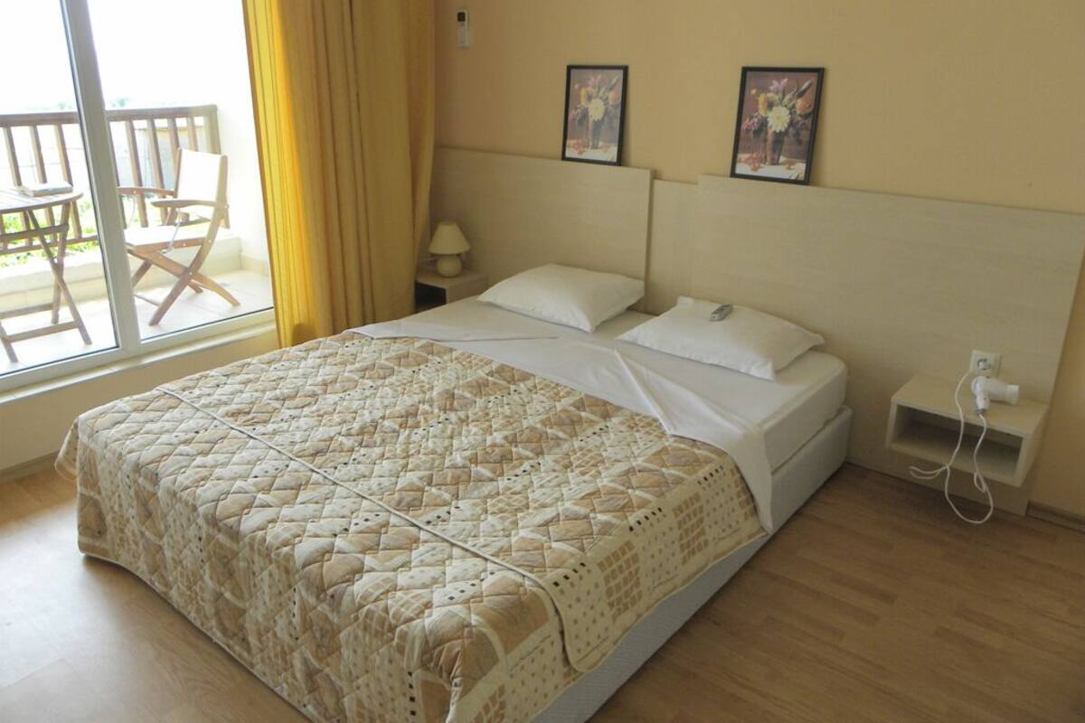 A bedroom with a large bed, a nightstand, a lamp, and a power outlet.