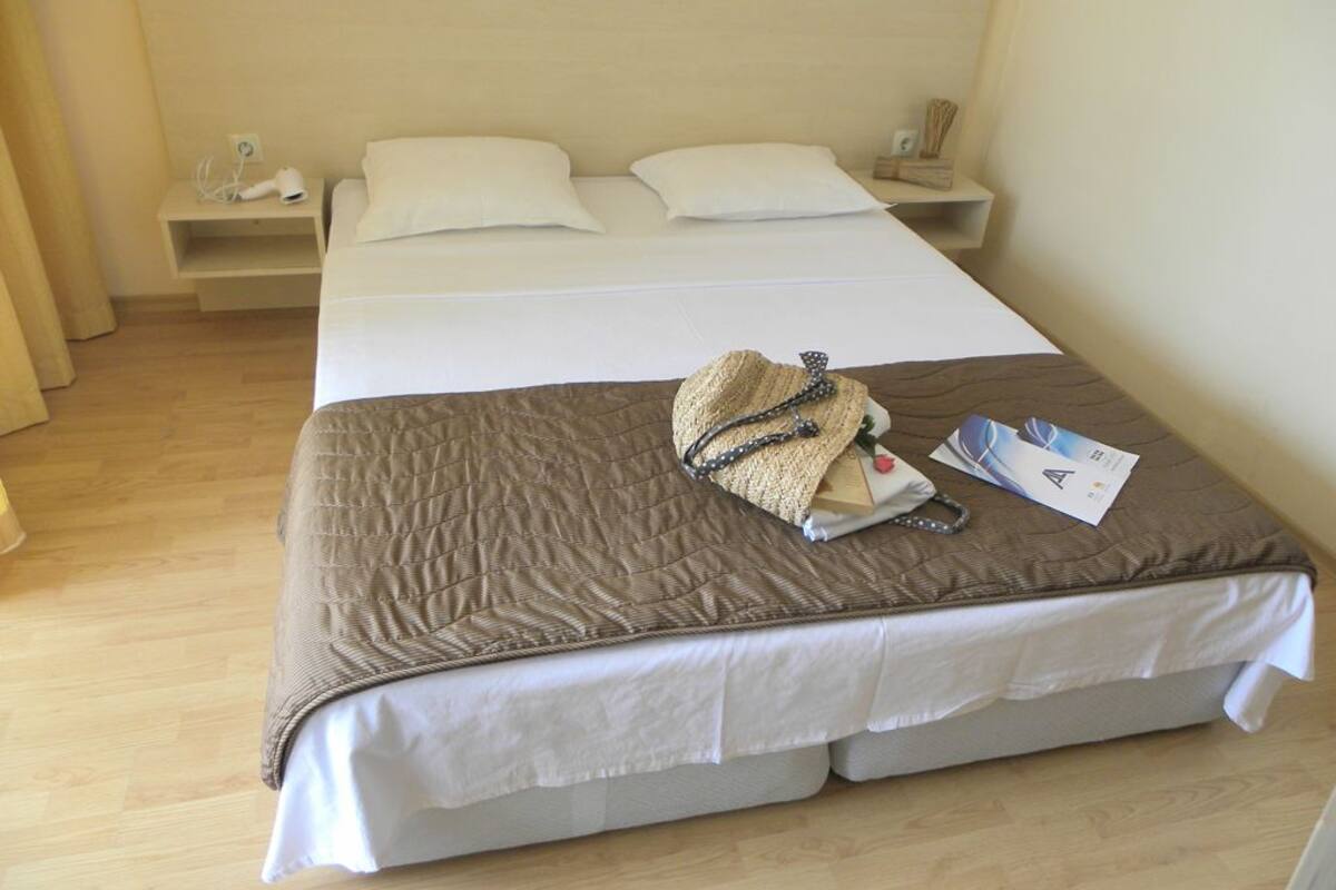 A neatly made bed with a brown quilt, a straw hat, a bag, and a magazine on it.