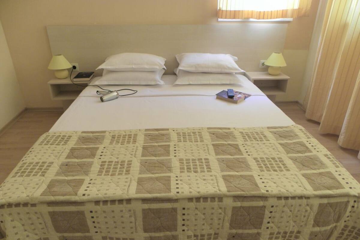 A neatly made bed with a quilt, two bedside tables with lamps, and a window with curtains.