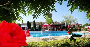 A swimming pool with lounge chairs, a gazebo, and a building with a red roof in the background. - Harmony Hills Residence (Balchik)