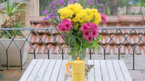 Une table en bois blanche, sur laquelle se trouve un vase jaune rempli de fleurs et deux tasses blanches.
