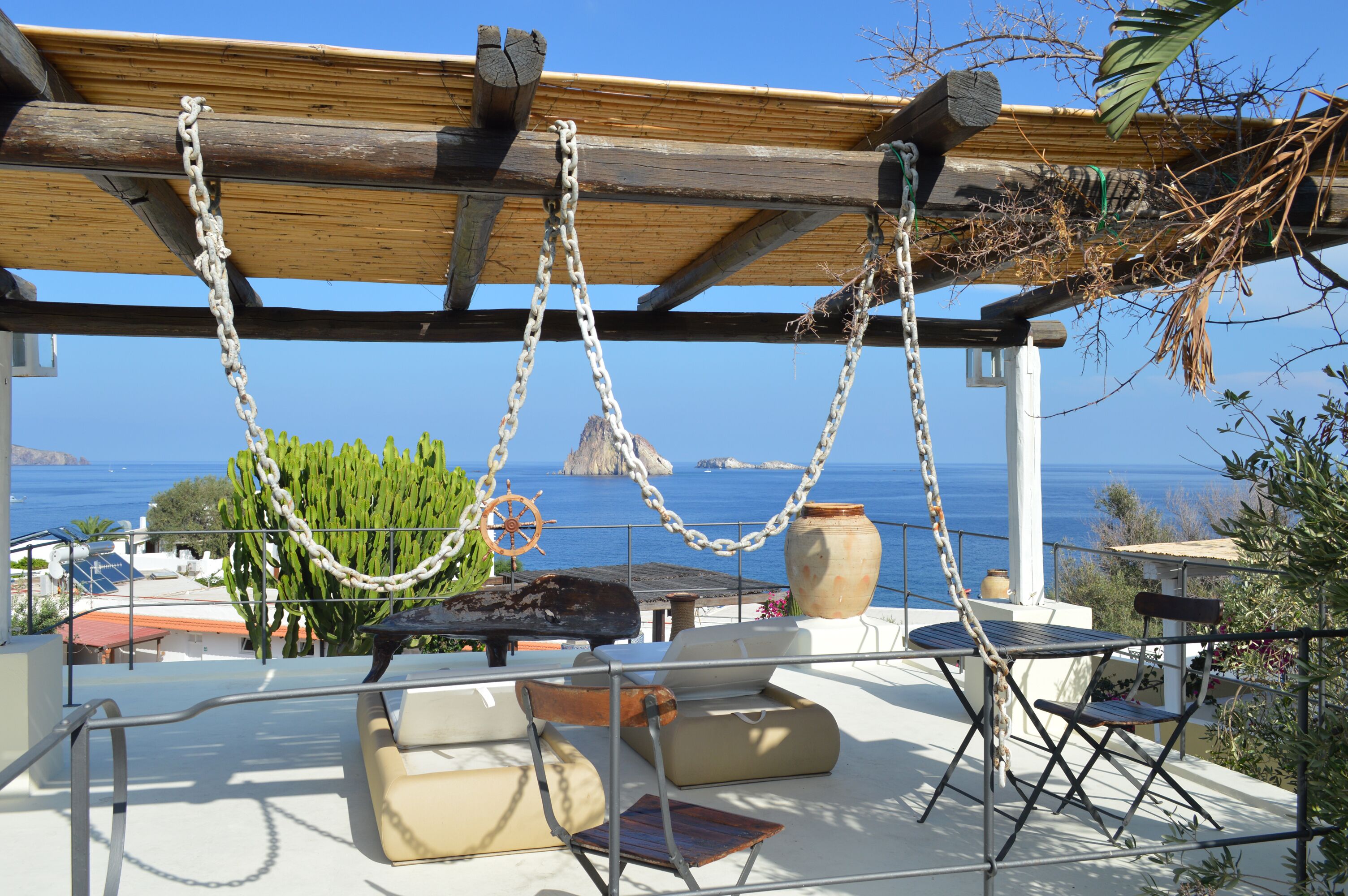 Een terras met uitzicht op zee, een houten pergola, ketting en buitentafels en -stoelen.