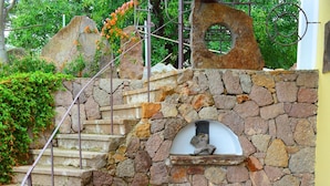 A stone staircase with a metal railing, leading to a stone wall with a circular window. - Casa Ambra (Lipari)