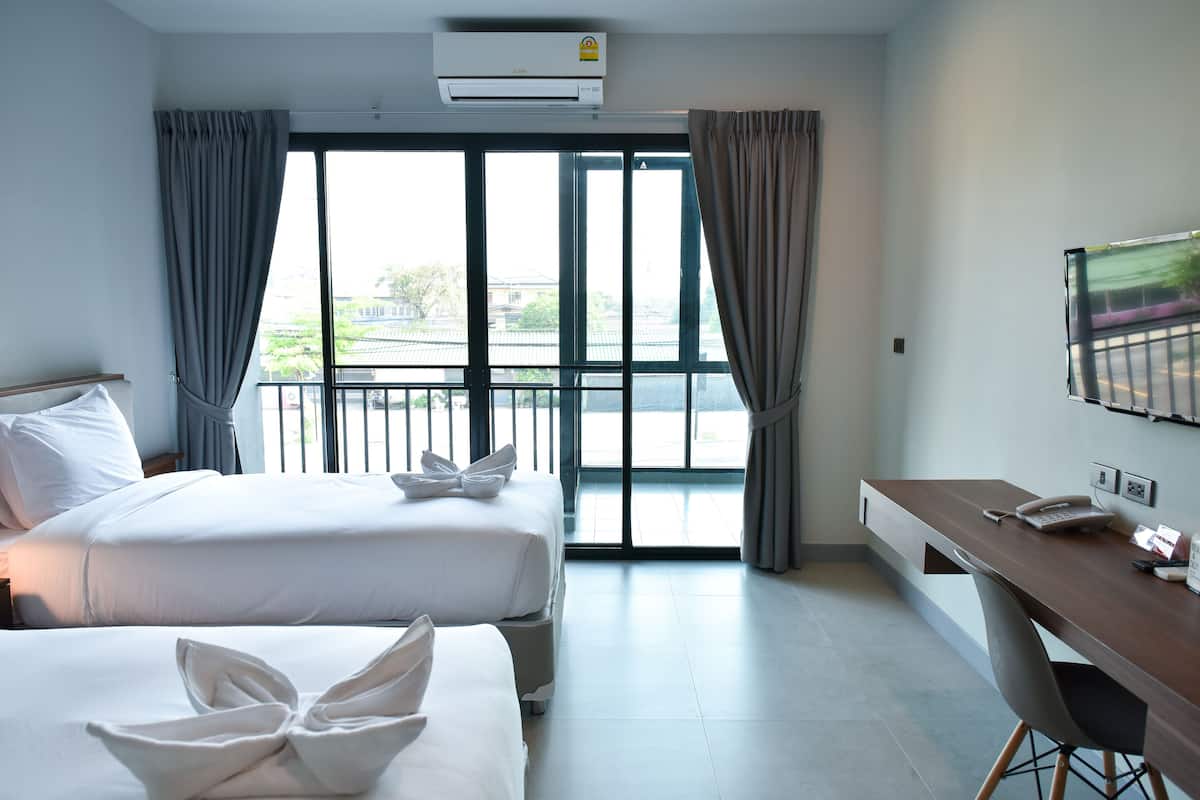 Habitación de hotel con dos camas, un escritorio, un televisor y un balcón con cortinas.