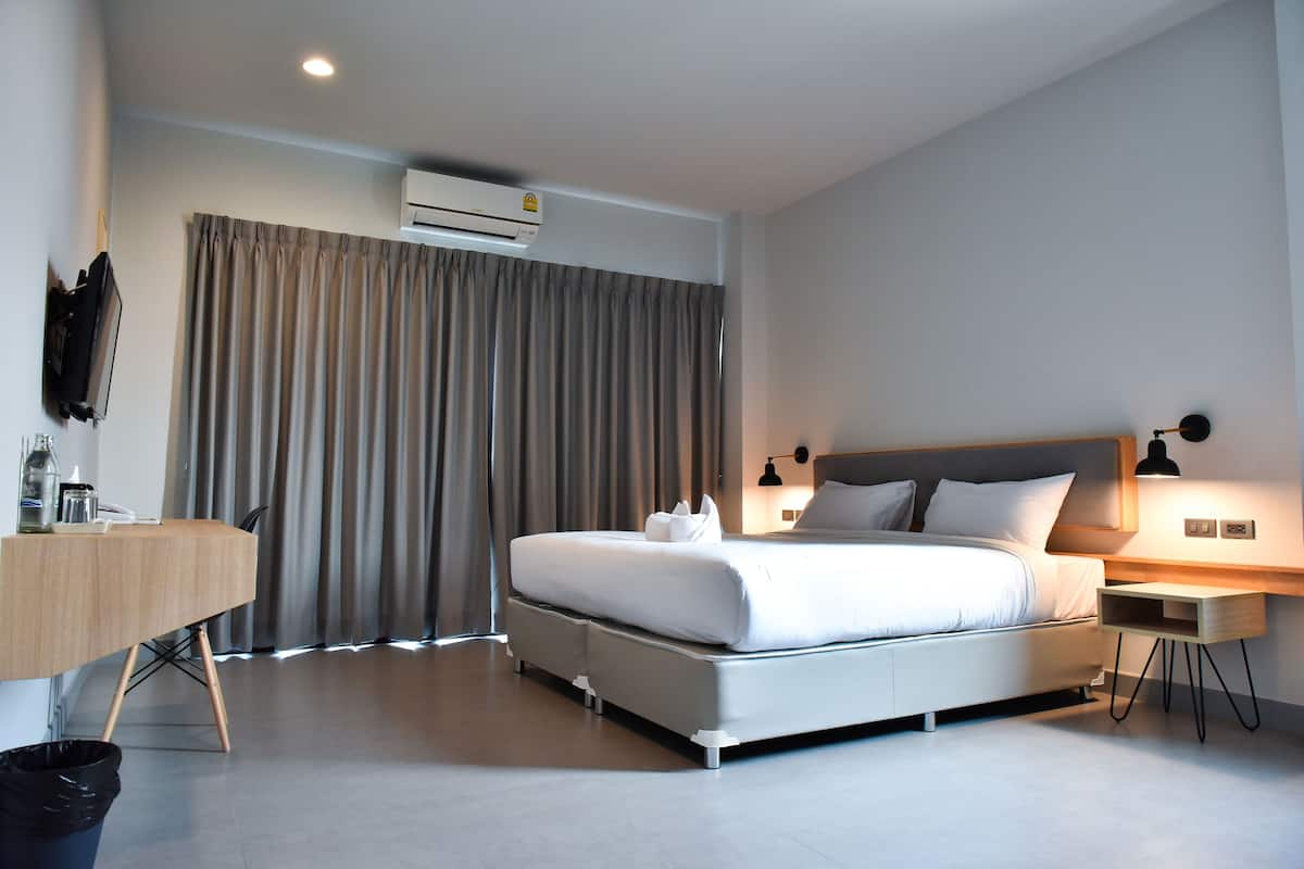 Una habitación de hotel moderna con una cama grande, mesitas de noche, un escritorio y un equipo de aire acondicionado.