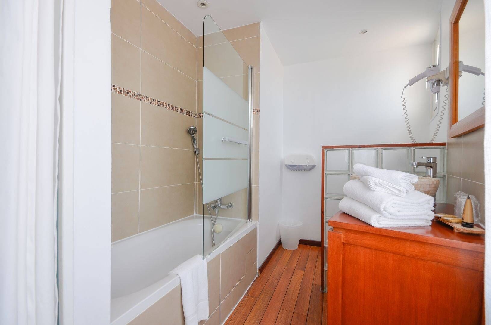 Un baño con ducha de vidrio, tocador de madera con toallas y un lavabo blanco.