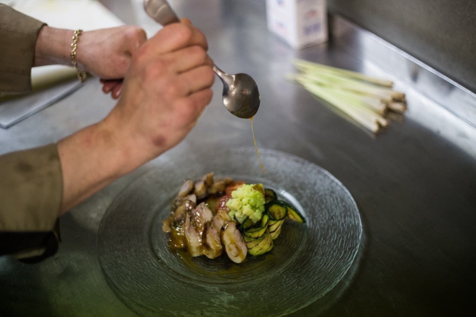 A person pouring sauce over a dish of sliced meat and vegetables.