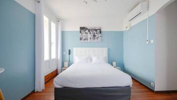 A bedroom with a large bed, a white headboard, a mounted picture, a bedside table, and an air conditioning unit.