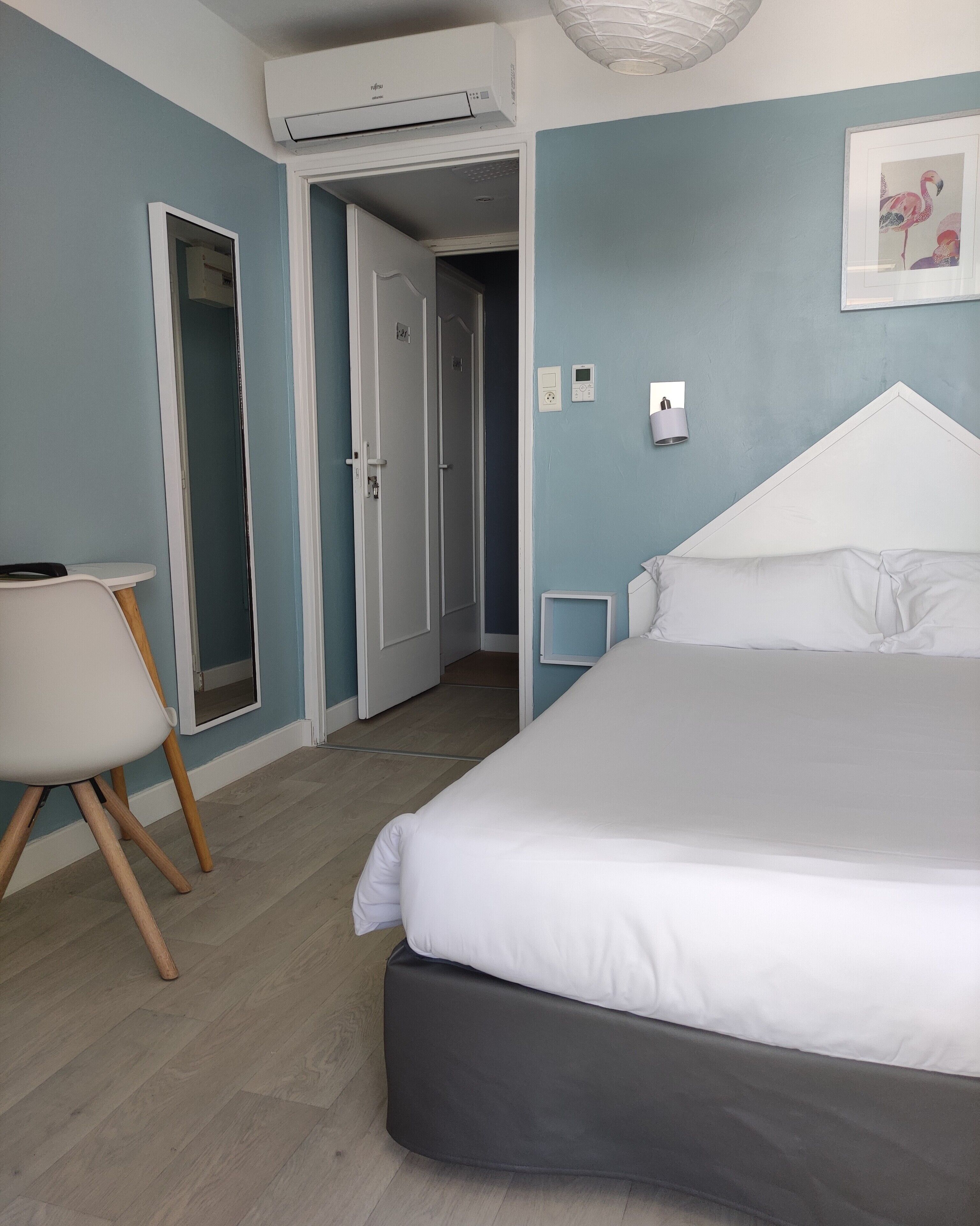 A bedroom with a bed, a chair, a desk, and a door leading to another room.