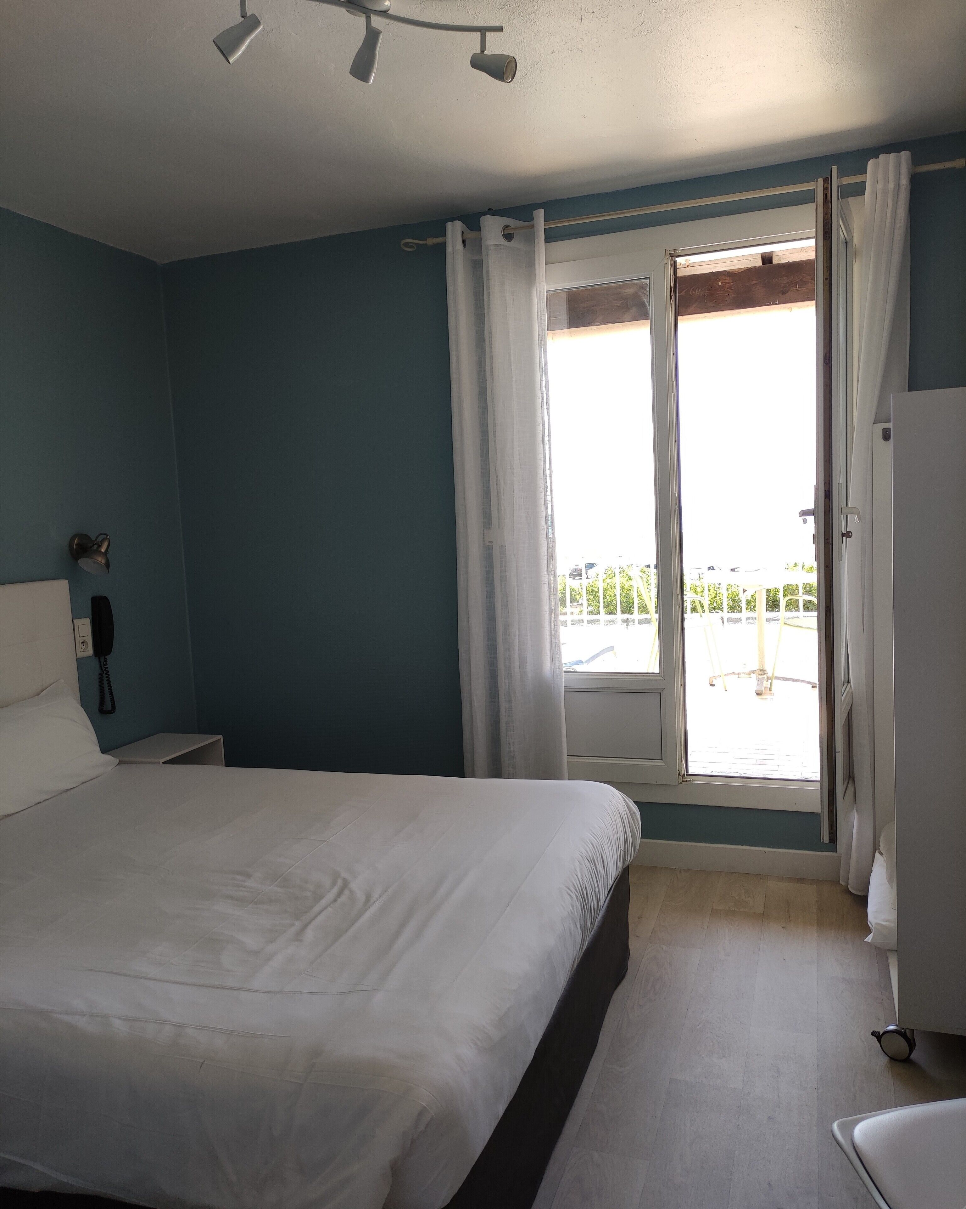 Ein Schlafzimmer mit einem Bett, einem Nachttisch, einem Telefon und einem Fenster mit Vorhängen.
