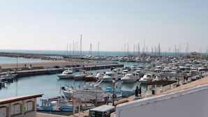 Uma marina com vários barcos atracados, uma praia de areia e céu claro.