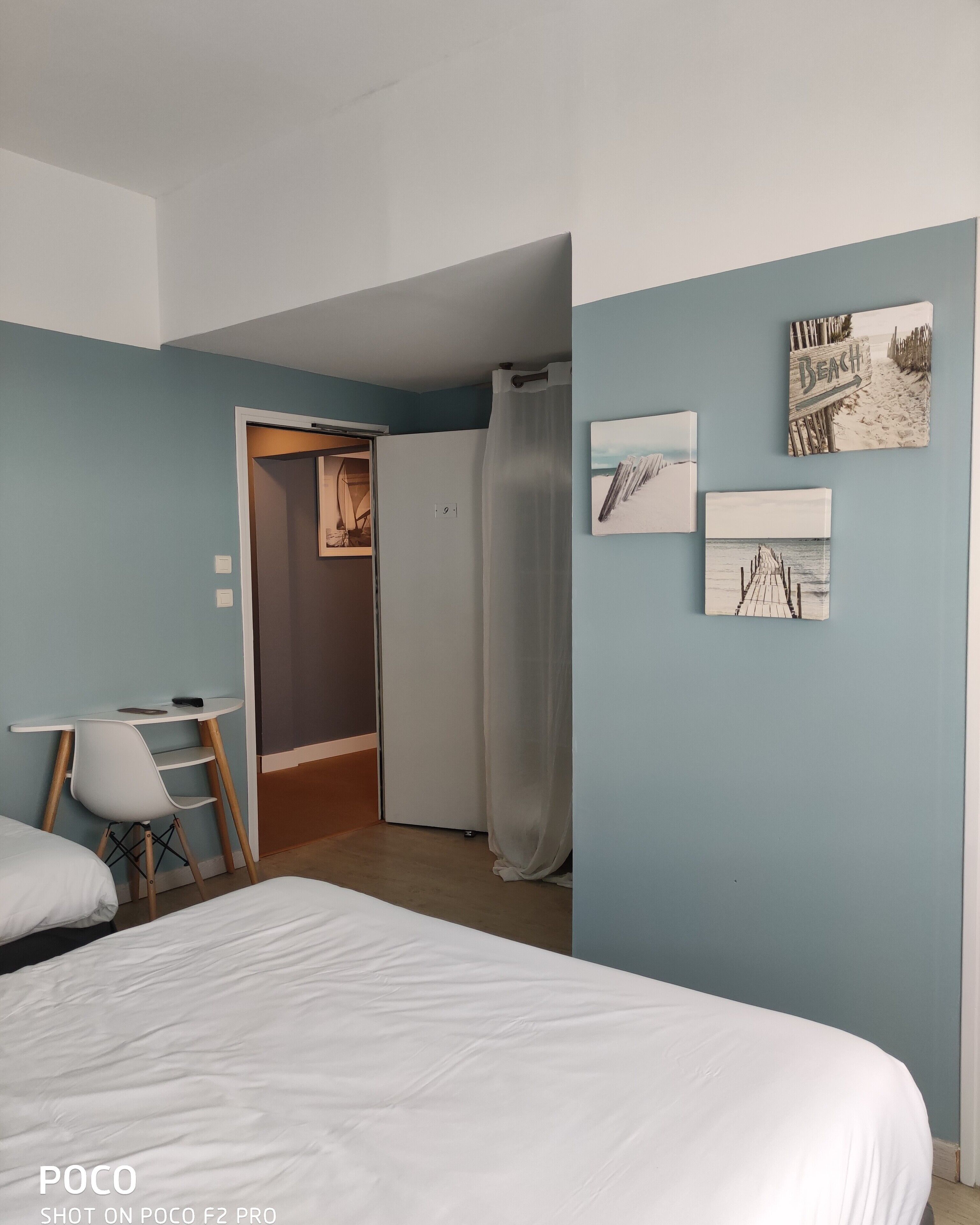 A bedroom with a bed, a desk, and a wardrobe. There are three wall art pieces depicting beach scenes.