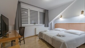 A bedroom with a bed, a desk, a chair, a TV, and a window with curtains. - Antica Residence (Kraków)