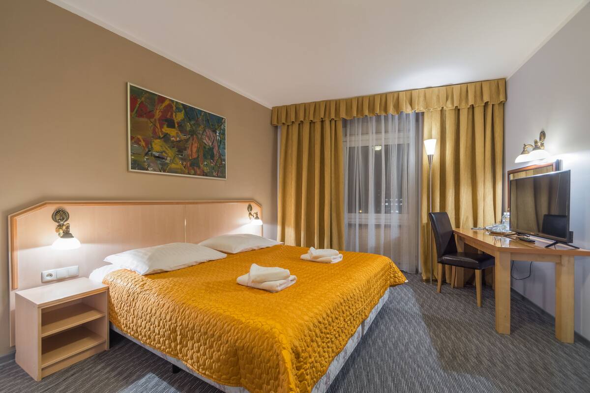 Una habitación de hotel con una cama grande, un escritorio con silla, un televisor y un cuadro en la pared.