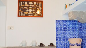 A kitchen with a tiled backsplash, a framed picture on the wall, and a countertop with cups and a teapot.