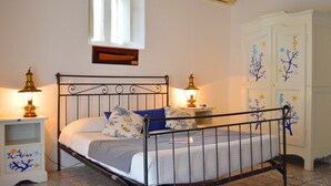 A bedroom with a metal bed frame, white walls, a window, a white wardrobe, and two bedside tables with lamps.