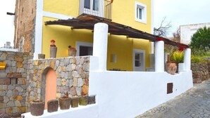 A yellow building with a stone wall, a balcony, and potted plants.