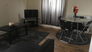 A living room with a sofa, a coffee table, a TV, and a dining table with chairs. - Majesty Tweed Apartment (Dundee)