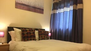 A neatly made bed with white bedding and patterned pillows, a bedside lamp, and a painting on the wall. - Majesty Tweed Apartment (Dundee)