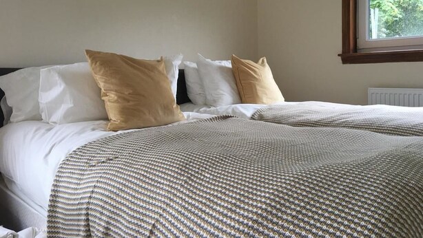 A bed with white and beige bedding, a patterned blanket, and a wall-mounted picture. - Majesty Tweed Apartment (Dundee)