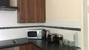 A kitchen with wooden cabinets, a microwave, toaster, and a kettle. - Majesty Tweed Apartment (Dundee)