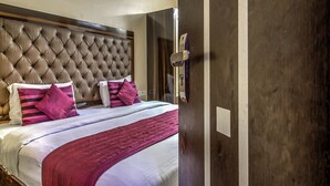 A hotel room with a tufted headboard, a large bed with a white and pink striped bedspread, and a wooden door with a handle. - OYO 2807 Hotel Crosswinds Residency (Noida)