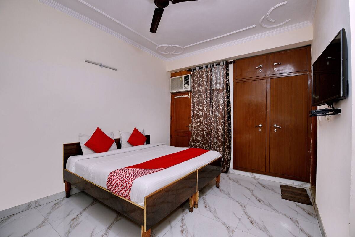 A bedroom with a bed, wooden wardrobe, a ceiling fan, and a television mounted on the wall.