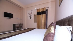 A hotel room with a bed, a TV mounted on the wall, a small table with chairs, and a window with curtains. - OYO 8907 The Nest (Greater Noida)