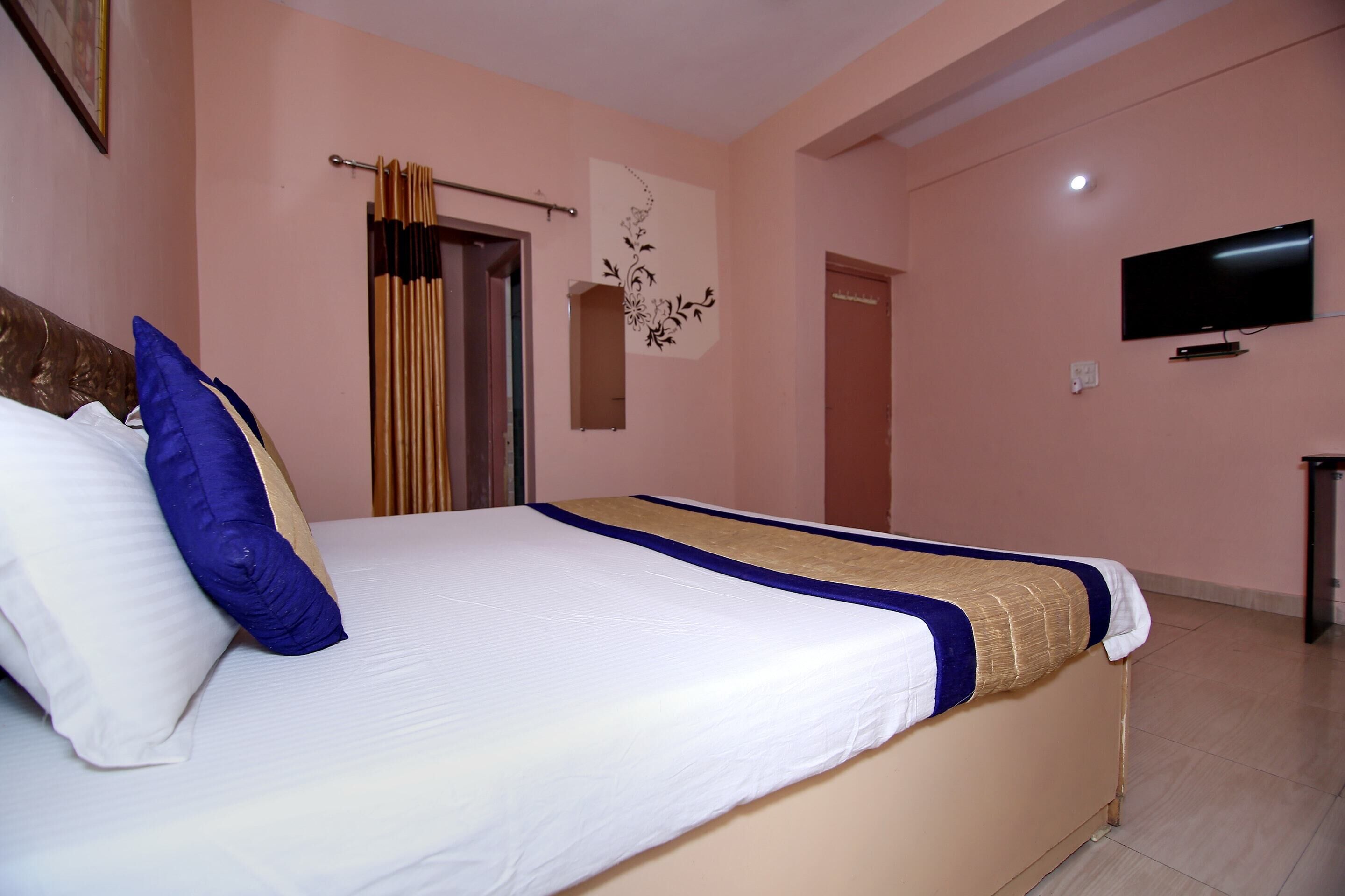 A neatly made bed with a white and blue bedspread, a blue pillow, and a beige accent. A flat-screen TV is mounted on the wall to the right.