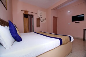 A neatly made bed with a white and blue bedspread, a blue pillow, and a beige accent. A flat-screen TV is mounted on the wall to the right. - OYO 8907 The Nest (Greater Noida)