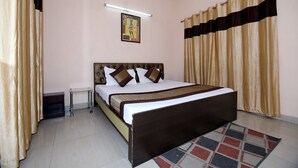 A bedroom with a bed, curtains, a bedside table, and a wall-mounted light fixture. - OYO 8907 The Nest (Greater Noida)
