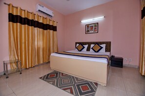 A bedroom with a bed, curtains, an air conditioner, a bedside table, and a wall-mounted picture. - OYO 8907 The Nest (Greater Noida)