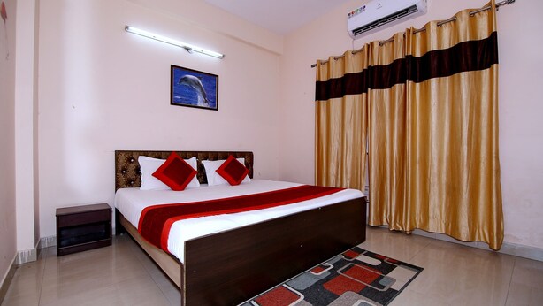 A bedroom with a bed, a nightstand, a wall-mounted air conditioner, a ceiling light, a framed picture, and a curtain. - OYO 8907 The Nest (Greater Noida)