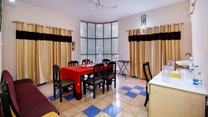 A dining area with a red table, chairs, a ceiling fan, and a window with curtains. - OYO 8907 The Nest (Greater Noida)