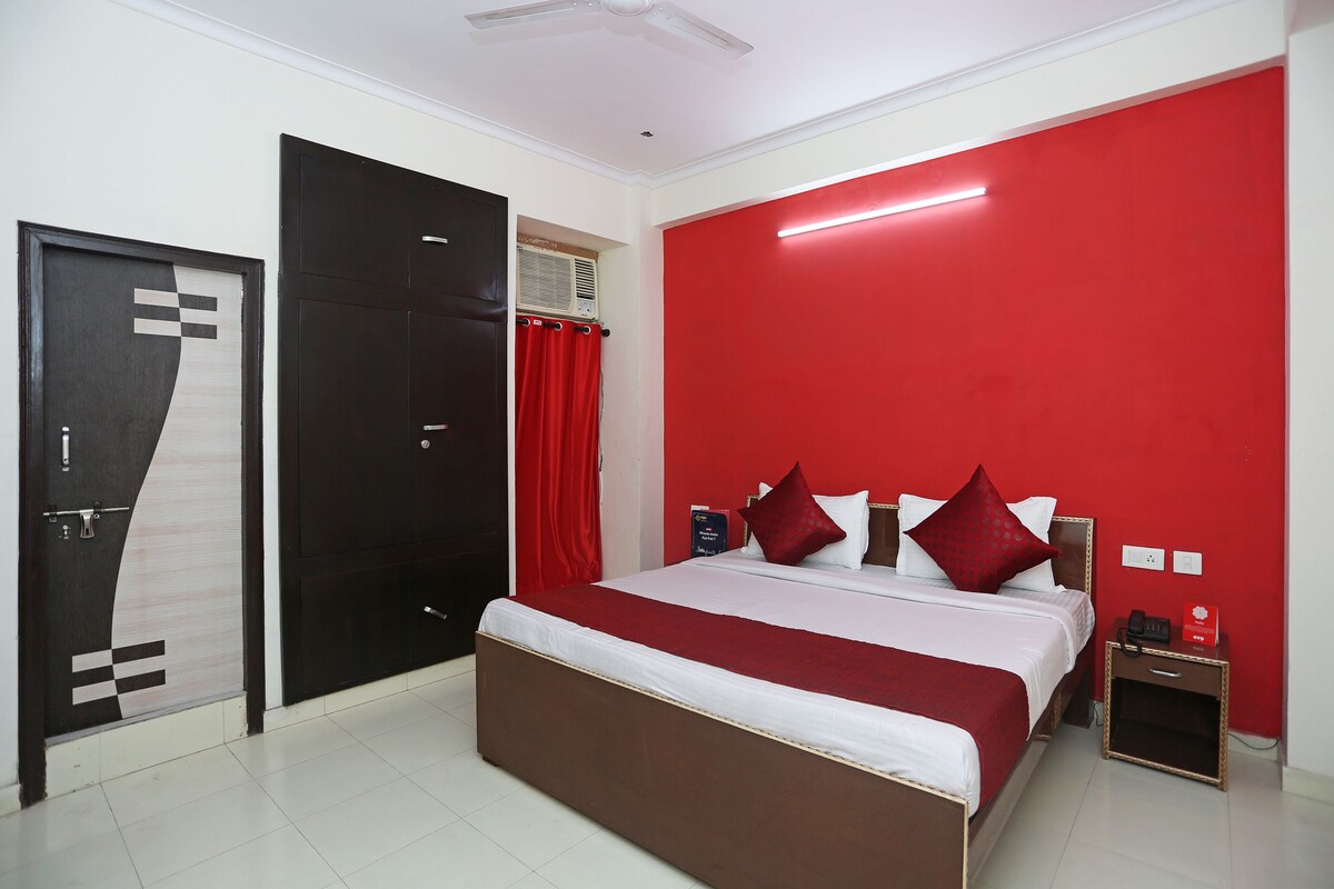 A hotel room with a large bed, a wardrobe, a nightstand, and a red accent wall.