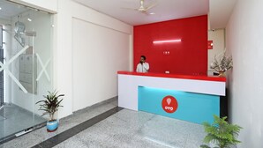 A reception area with a red and blue desk, a ceiling fan, and a potted plant. - OYO 9339 Terrene Empire (Noida)