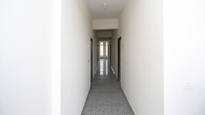 A narrow, well-lit hallway with a polished floor, leading to a door at the end. - OYO 9339 Terrene Empire (Noida)