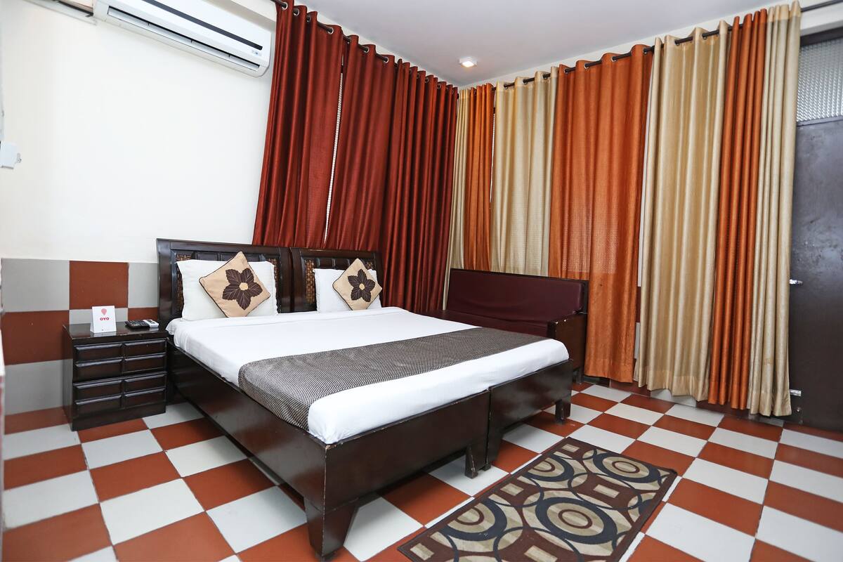 A hotel room with a bed, a nightstand, a dresser, and a patterned rug.