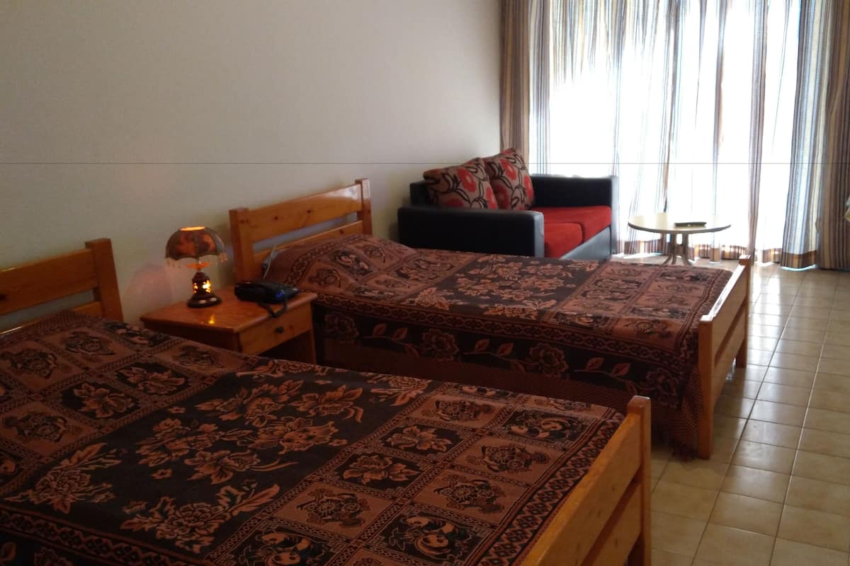 A hotel room with two beds, a small table, a sofa, and a television.