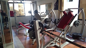 Un gimnasio con diversos equipos de ejercicio, incluyendo una prensa de banca, una prensa de piernas y una máquina de poleas.