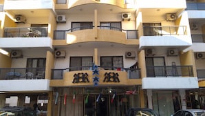 Un edificio de varios pisos con balcones, unidades de aire acondicionado y una fachada con banderas.