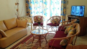 Una sala de estar con un sofá, dos sillas de mimbre, una mesa de centro de vidrio y un televisor.
