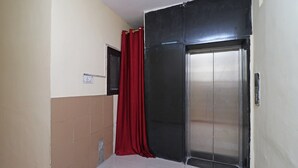 A narrow hallway with a red curtain, a tiled wall, and a closed elevator door. - OYO 10661 DSR Classic (Noida)