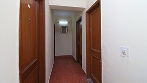 A narrow hallway with wooden doors on both sides, a tiled floor, and a light switch on the wall. - OYO 10661 DSR Classic (Noida)