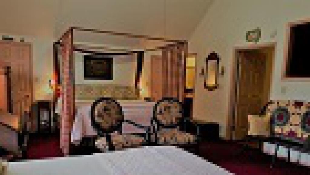 A four-poster bed with a canopy, a desk with a chair, and a small table with a chair in a hotel room.